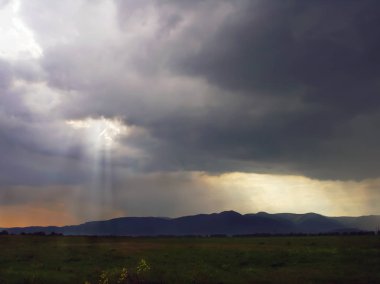 Karpat dağlarının arka planında yağmur sırasında güneşin ışınları gök gürültülü bulutlar aracılığıyla kırmak