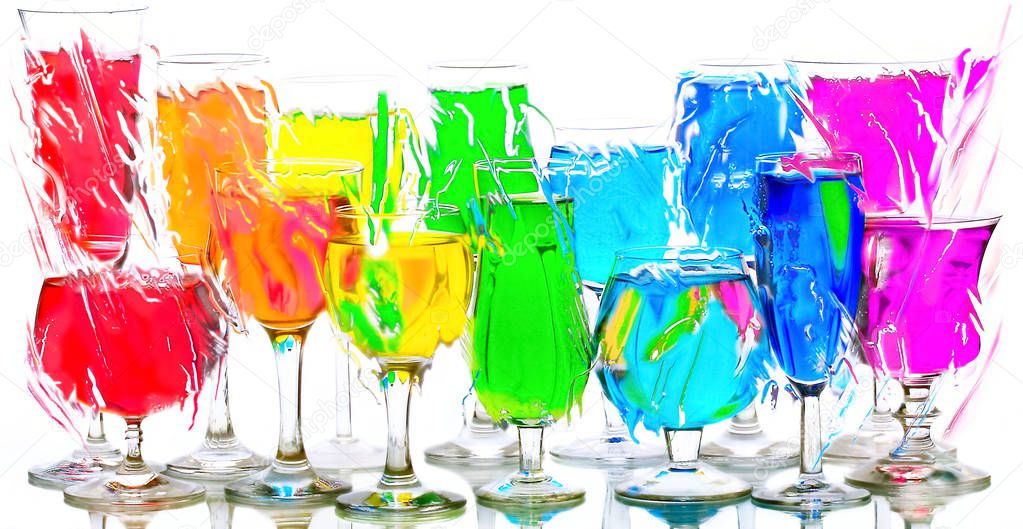 Wine glasses with red, orange, yellow, green, blue, violet liquids stand on a glass surface on a white background