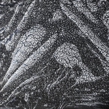 Donmuş akan yağmur damlaları ve yuvarlak buz parçacıkları siyah cam bir yüzey üzerinde yer alır. Yakın plan..