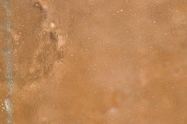 Doku. Açık kahverengi arka planda ince eriyen buz tabakasıyla kaplı bir cam yüzey parçası bulunur. Yakın plan..