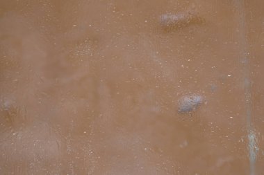 Eriyen ince bir buz tabakasıyla kaplı cam bir yüzey parçası, sütlü kahvenin arka planında yer almaktadır. Yumuşak odak.