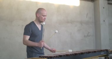 Gri endüstriyel arka planı olan gri elbiseli bir adamın başı ve vücudu marimba çalıyor.