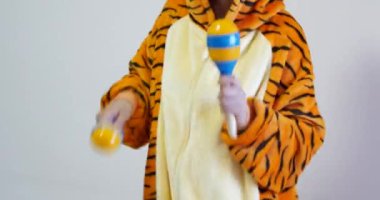 Marakas çalan tanınmamış kadın öğretmen tatlı kaplan kigurumi kıyafetleri giyiyor. Maracas genellikle müzik eğitimi için kullanılan bir vurmalı çalgıdır..