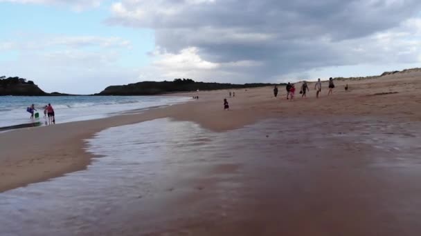 Letecký záběr nerozpoznatelného dítěte běžícího na pláži s lidmi kolem, dramatické modré nebe s mraky, granville, Francie, 19-8-19 — Stock video