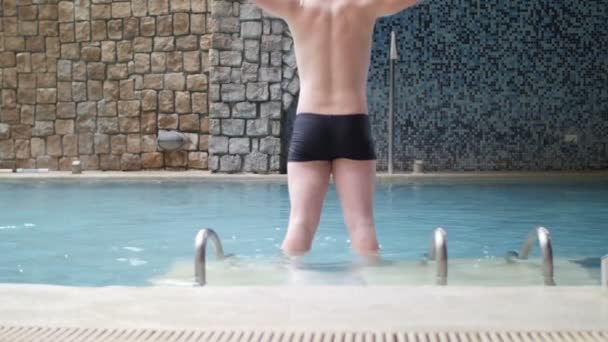 Hombre guapo saltando a la piscina con salpicaduras de agua en cámara lenta , — Vídeo de stock