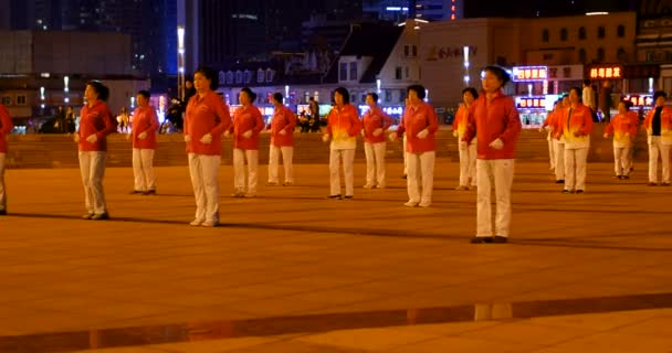 Vieilles dames à l'extérieur portant des uniformes rouges, danse synchronisée pour la nouvelle année, les personnes âgées chinoises dansant la nuit. panneaux en chinois derrière : restaurant de nouilles, restaurant barbecue et supermarché — Video