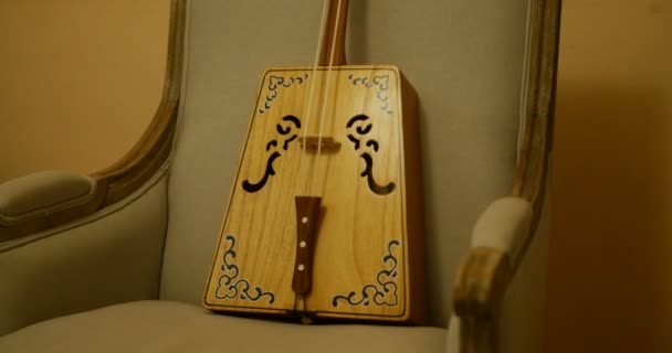 Close shot de ma tout qin, instrumento de música tradicional chinesa cordas mongóis. tradicional de madeira feita objeto situado em uma poltrona cinza estilo antigo com parede amarela, estilo tranquilo e surpreendente — Vídeo de Stock