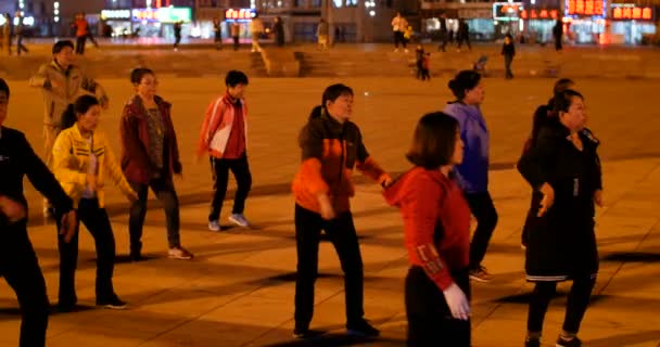 Damas de edad media bailando para el evento de año nuevo en la noche al aire libre en una gran plaza llena de gente, carteles en chino detrás: restaurante de fideos, restaurante barbacoa, y supermercado Dalian, China - Febrero 2019 — Vídeo de stock