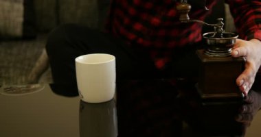 Kahve çekirdeklerini antika kahve öğütücüsüne koyan adam kırmızı ve siyah kareli hippi tişörtü giyiyor.