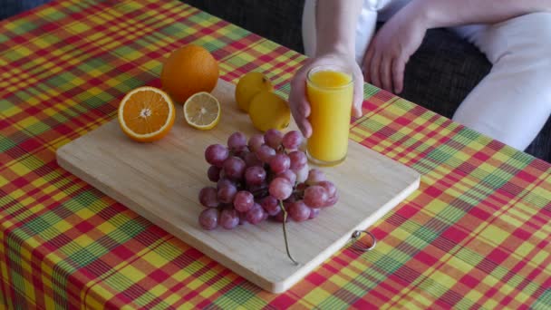 新鮮な有機オレンジ 柑橘類 グレープフルーツ スイカとガラスの中に新鮮な圧搾汁とテーブルからオレンジジュースのガラスを取る男 — ストック動画
