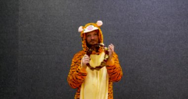 Kigurumi giymiş, kaplan kostümü giymiş ve tef çalan komik gülümseyen bir adamın yarı vücut fotoğrafı. Profesyonel bir müzisyen için çok komik bir tutum..
