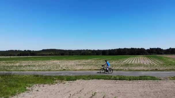 空気:認識できない男は、緑の電気自転車に大きな牧草地を横断する単一の歩道をスピードダウンします。風光明媚な田園地帯で下り坂のサイクリングで彼の一日を楽しむアスレチック男性観光客. — ストック動画