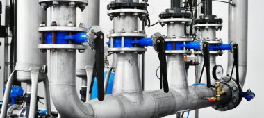 Büyük endüstriyel su arıtma ve kazan dairesi. Parlak çelik borular, mavi pompalar ve vanalar..