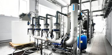 Büyük endüstriyel su arıtma ve kazan dairesi. Parlak çelik borular, mavi pompalar ve vanalar..