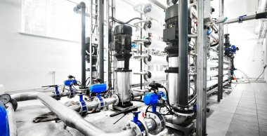 Büyük endüstriyel arıtma tesisi ve kazan dairesi. Parlak çelik metal borular ve mavi pupms ve vanalar.