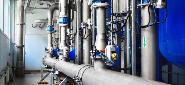 Büyük endüstriyel su arıtma ve kazan dairesi. Parlak çelik borular, mavi pompalar ve vanalar..