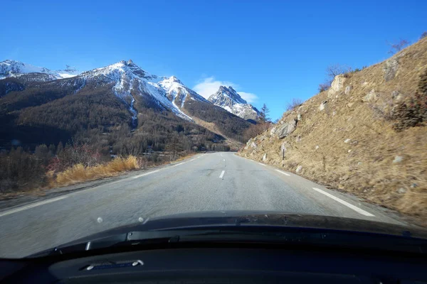 A view from the car on an asphalt road in French Alps mountains near Parc Ecrins on a clear day