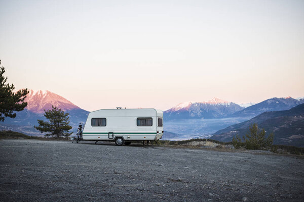 Caravan with a bike parked on a mountaintop with a view on the french Alps near lake Lac de Serre-Poncon