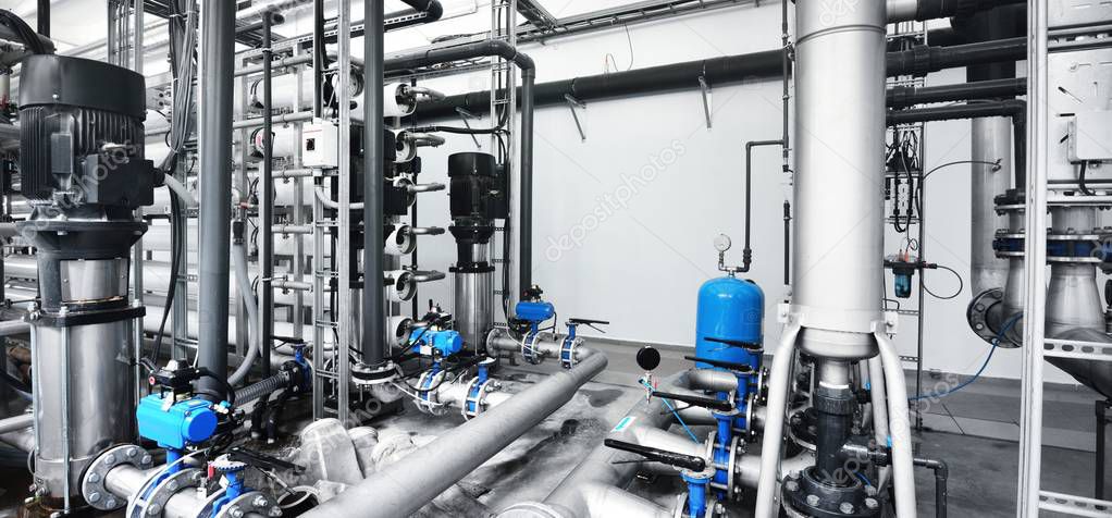 Large industrial water treatment and boiler room. Shiny steel metal pipes and blue pumps and valves.