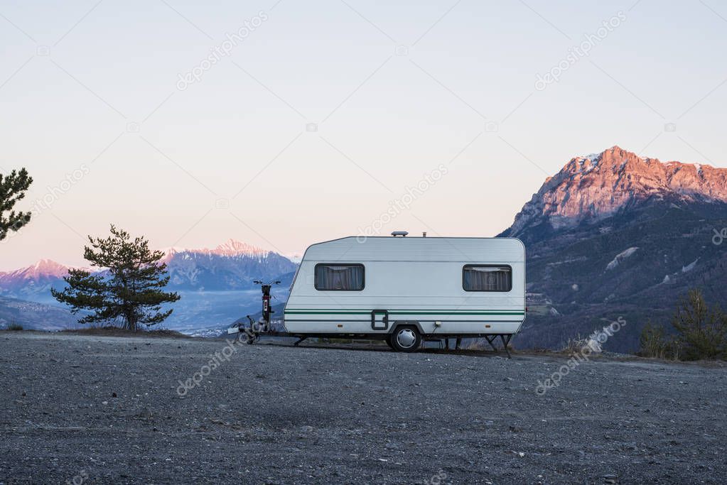 Caravan with a bike parked on a mountaintop with a view on the french Alps near lake Lac de Serre-Poncon