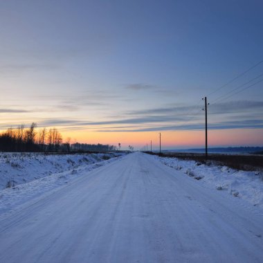 Gün batımında kar altında bir kış gününde telgraf direkleri olan kırsal yol