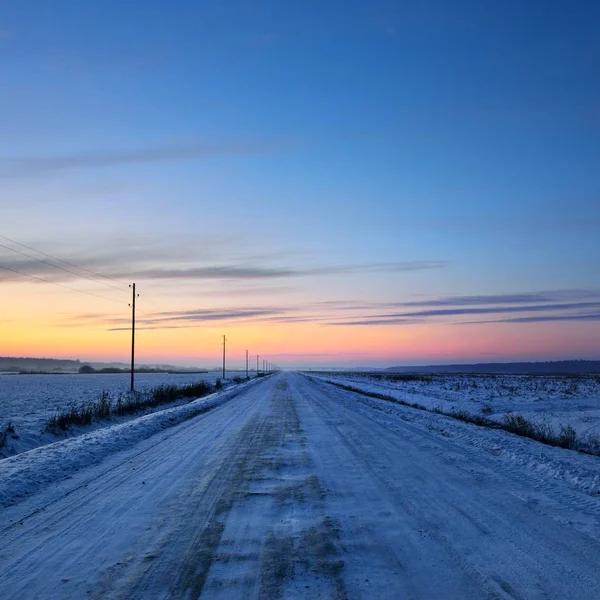 積雪下で夕暮れ時の冬の日の電柱と田舎道 — ストック写真