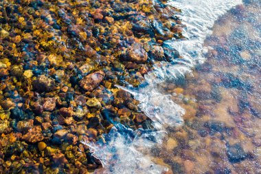 Denizin donmuş suyunun altında renkli taşlar, Letonya