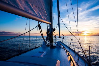 Sailing at sunset. A view from the yacht's deck to the bow and sails, Baltic sea, Latvia clipart