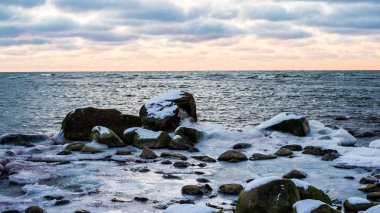 Kış manzarası. Gün batımında Baltık denizinin karla kaplı taşlı deniz kıyısı. Paldiski, Estonya