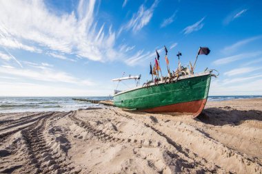 Güneşli bir günde bulutlu mavi gökyüzü altında Baltık deniz kıyısında ve denizde eski bir ahşap tekne, Letonya