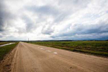 Güneşli bir sonbahar gününde ülkenin tarımsal kültür alanlarında toprak bir yol. Fırtınalı mavi gökyüzü. Letonya