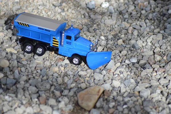 Blue toy snow removal truck on gravel.