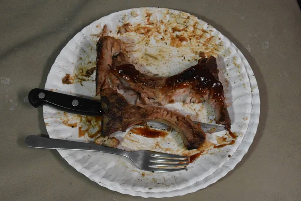 Çoğunlukla bıçak ve çatal ile beyaz kağıt tabak üzerinde domuz pirzolası yemiş.