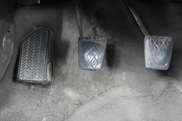 Car gas pedal, brake pedal, and clutch pedal on car floor.