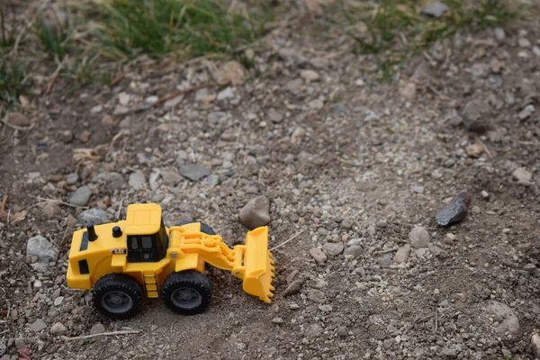 Çimenli çakıl üzerinde oyuncak sarı inşaat oyuncağı.