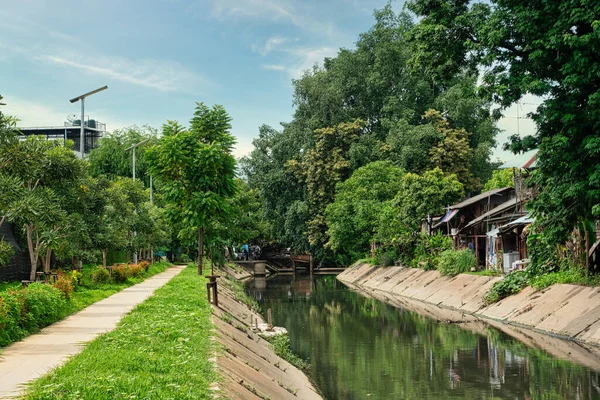 Sığ kanal, huzurlu yürüyüş yolu, ağaçlar ve kanal boyunca evler. Kanal boyunca bir yürüyüş yolu huzurlu bir köye girer..