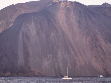 Yanardağın eteğinin denize düşmesi, yakınlarda tekneler.