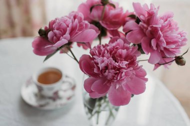 Masada pembe şakayıklar ve bir fincan çay.