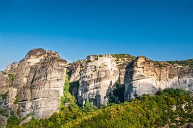 Meteora Yunanistan Manastırı. Göz kamaştırıcı panoramik manzara. Bulutlu destansı mavi gökyüzüne karşı dağlar ve yeşil orman manzarası. Unesco miras nesnesi.