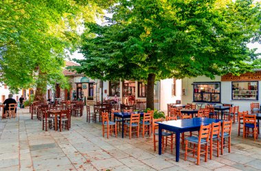 Lafkos / Yunanistan - 4 Temmuz 2020: Köyün tarihi meydanının manzarası, kafeteryalar ve restoranlar ve çok sayıda uçak ağacı.