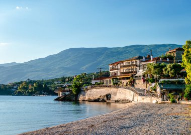 Afissos / Yunanistan - 23 Mayıs 2020: Deniz kenarında evleri ve arka planda Pelion dağı olan köyün rıhtım manzarası.