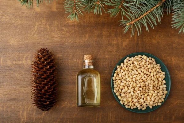 Cedar products: cedar oil in glass bottle, pine nuts, cone, brunches on a wooden broun background. Top view.