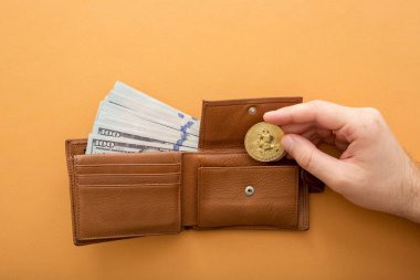 Turuncu arka planda Bitcoin, yüz dolarlık banknotlar ve deri cüzdan.