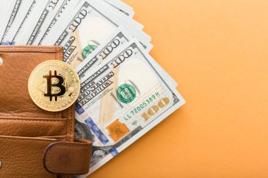 Turuncu arka planda Bitcoin, yüz dolarlık banknotlar ve deri cüzdan.