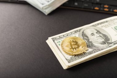 Close up shot gold Bitcoin on dollar banknote over computer on black background.