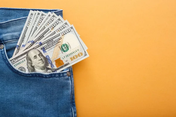 Dolarach amerykańskich w kieszeni dżinsy na pomarańczowym tle. — Zdjęcie stockowe