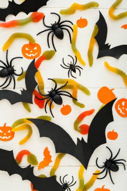 Tatlı şeker, solucanlar, kağıt yarasalar, örümcekler, beyaz ahşap arka plan papalık kabakile Cadılar Bayramı arka plan. Cadılar Bayramı tatil süslemeleri. Düz döşeme, üst görünüm.