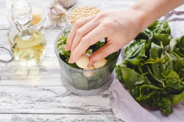 Beyaz ahşap masada peynir, çam fıstığı, zeytinyağı, fesleğen, sarımsak bir blender pesto sos yapma işlemi. Eko kavramı, sağlıklı beslenme, çevre dostu, sağlıklı co