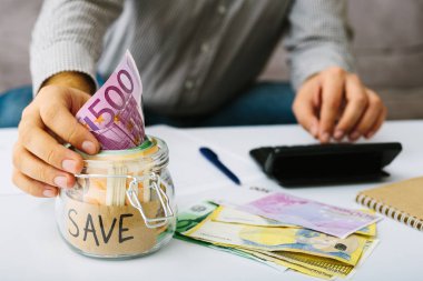 İnsanların eli tasarruf için bir cam şişeye euro banknot koyarak. Adam muhasebesini yapıyor. Küçük işletmeler: mevduat ve borç verme, faiz oranı azaltma.