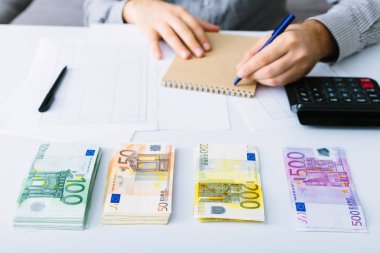 Euro banknotlar istiflenir. Adam muhasebesini yapıyor. Küçük bir işletmede giderlerin dağıtımı. Tasarruf, mevduat, borç verme ve faiz oranı.